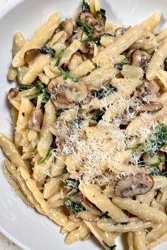 pasta with mushrooms, spinach and parmesan cheese in a white bowl on a table