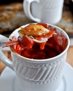 a spoon full of food sitting in a cup on top of a saucer next to a plate