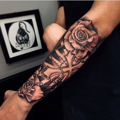 a man with a black and grey tattoo on his arm holding a clock in the shape of a rose