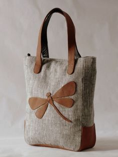 a handbag with a dragonfly on the side and brown leather handles, sitting on a white surface