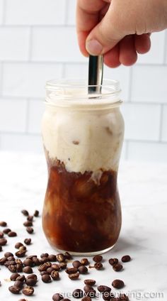 a hand is holding a spoon in a jar filled with coffee beans and ice cream