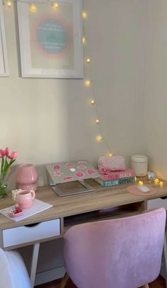 a desk with two pink chairs and some lights on the wall behind it in a bedroom