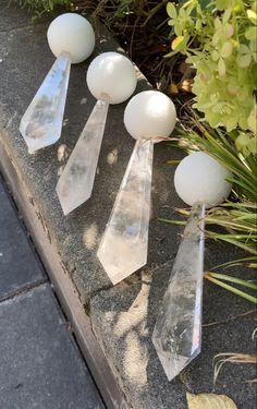 four clear glass ornaments sitting on top of a cement slab next to plants and flowers