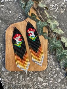 a pair of earrings on top of a wooden board next to a plant with leaves