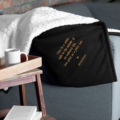 there is a blanket on the back of a couch next to a coffee cup and book