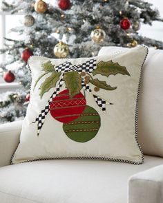 a christmas tree is in the background behind a white couch with a red and green ornament on it