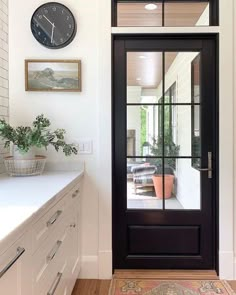 a clock is on the wall next to a black door in a white room with wood floors