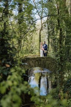 a bride and groom standing on a bridge in the woods