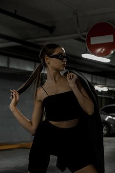 a woman wearing sunglasses and a black outfit in a parking garage with her hair pulled back