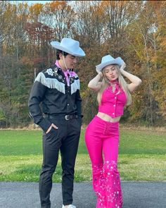 a man and woman in cowboy hats standing next to each other on a road with trees in the background