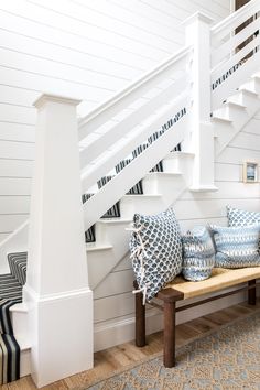 there is a bench with pillows on it next to the stairs in this house,