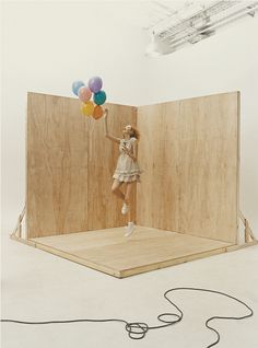 a woman holding balloons standing on top of a wooden platform in front of a wall