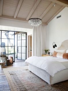 a large white bed sitting in a bedroom under a chandelier next to a doorway