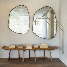 two circular mirrors on the wall above a wooden table with three small trays under them