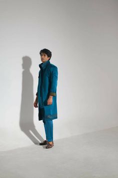 Featuring a teal overcoat with abstract hand paint detailing at the hem and collar. Paired with a tone on tone shirt kurta and tapered trousers. Blue Nehru Jacket For Fall With Long Sleeves, Fitted Blue Nehru Jacket For Fall, Traditional Blue Kurta For Fall, Blue Nehru Jacket For Festive Workwear, Festive Blue Nehru Jacket For Work, Festive Blue Nehru Jacket For Workwear, Blue Long Sleeve Kurta For Winter, Blue Long Sleeve Kurta For Fall, Blue Long Sleeve Winter Kurta