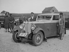 two men standing next to an old car