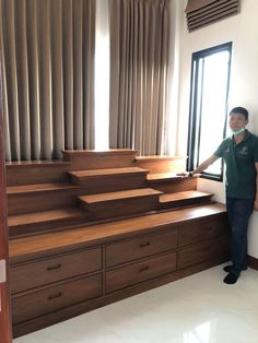 a man standing in front of a window next to wooden steps and drawers on the wall