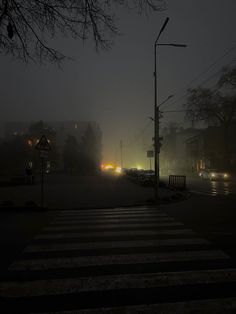 cars driving down the road at night in foggy weather with street lights and traffic signals