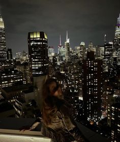 a woman standing on top of a building looking at the city lights in the distance