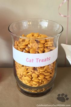 a glass bowl filled with cat treats sitting on top of a table next to a pink ribbon