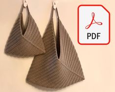 two knitted triangle shaped earrings hanging from hooks on a white wall with a red sign