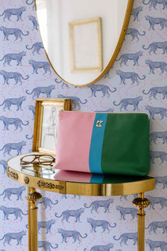 a pink, green and blue purse sitting on top of a table next to a mirror