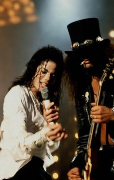 two men with long hair and hats are singing into microphones while one man in top hat is holding a microphone