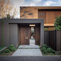 a modern house with wooden doors and brown siding on the outside, surrounded by greenery