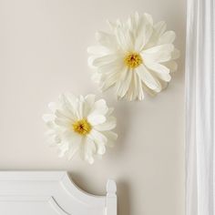 two large white flowers are on the wall above a bed with a white headboard