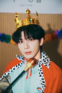 a young man wearing a crown and holding a cane in front of a wall with streamers