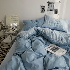 an unmade bed with blue comforter and pillows on it in a white room