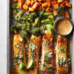 salmon, broccoli, and sweet potatoes on a baking sheet with dipping sauce