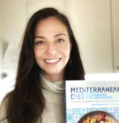 a woman holding up a book about the mediterranean diet