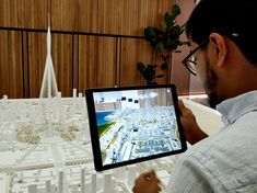 a man holding up a tablet with a city model on the screen in front of him