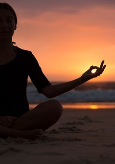 a woman is sitting on the beach with her hands in the air as the sun sets