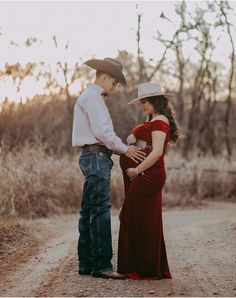 a pregnant woman in a red dress standing next to a man wearing a cowboy hat