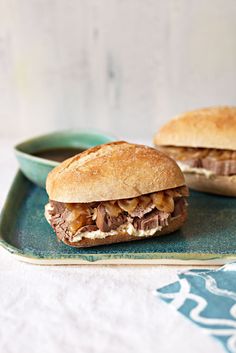 two sandwiches with meat and cheese on a green plate next to a bowl of dipping sauce