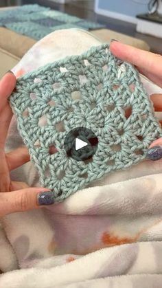 a woman is holding a crocheted square in her hands, with the video screen showing