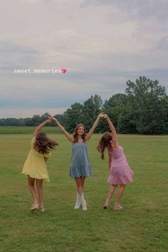 three young women standing on top of a grass covered field holding hands in the air