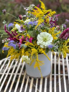 a white vase filled with lots of colorful flowers on top of a metal grill grate