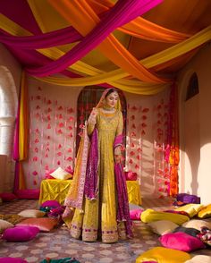 a woman in a yellow and pink outfit standing under a canopy with colorful drapes