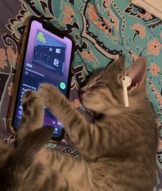 a cat laying on top of a bed next to an open cell phone with ear buds in it's ears