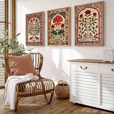 a white chair sitting next to a wooden dresser in a room with three paintings on the wall