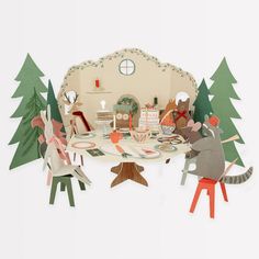 paper cut out of mice sitting at a table with plates and cups on it, surrounded by trees