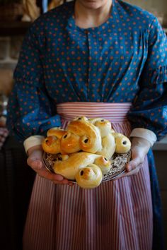 a woman in an apron holding a plate full of bread