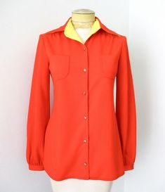 Groovy vintage 1960's or 70's tomato red textured polyester knit button front blouse from Crystal Collections. Features - navy blue stitching details - gold tone buttons - one button cuffs - chest pockets - straight hem - side splits APPROXIMATE MEASUREMENTS in inches - lying flat Size:  6 Shoulder to shoulder:  15 Sleeve, from shoulder:  23 Chest, armpit to armpit:  18 Waist:  17 Length, from shoulder:  27 CONDITION One front button is detached (it's pinned on).  Good vintage condition with lig Classic Orange Buttoned Top, Classic Orange Tops With Buttons, Retro Blouse With Buttons For Fall, Vintage Red Tops With Button Closure, Vintage Red Collared Blouse, Vintage Red Top With Button Closure, Red Collared Vintage Blouse, Vintage Orange Button-up Tops, Retro Collared Blouse With Buttons