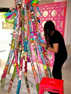 a woman standing next to a red chair near a colorful tree made out of crayons