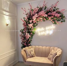 a couch sitting in front of a wall with flowers on it and a neon sign