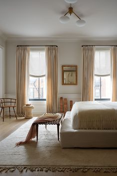 a large bed sitting under two windows in a bedroom next to a table and chair