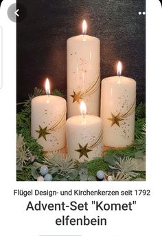 four white candles with gold stars on them and greenery in front of a black wall